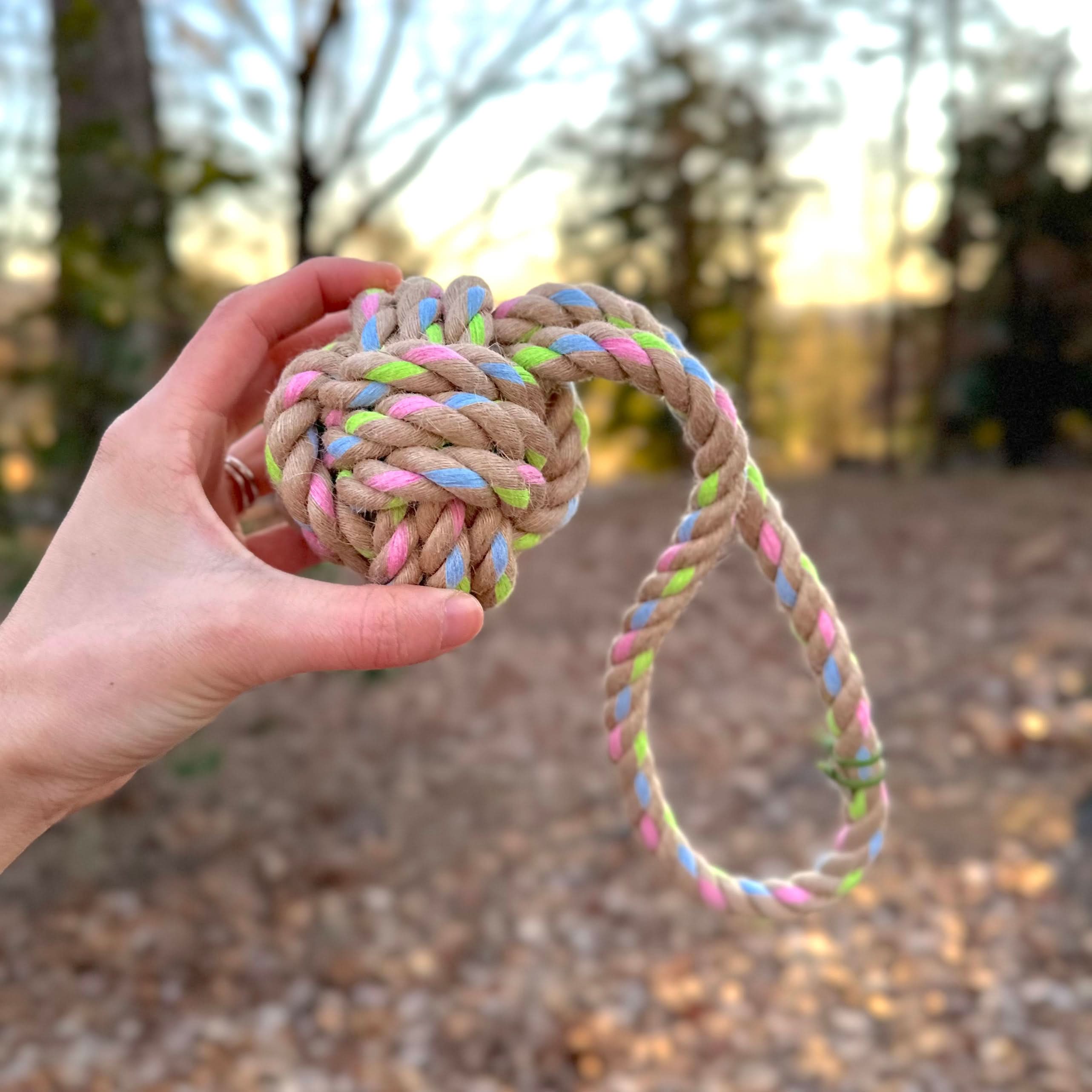 Hand holds a 12.5-inch Rainbow Joy hemp rope tug toy with blue, pink, green specks in natural hemp and recycled cotton.