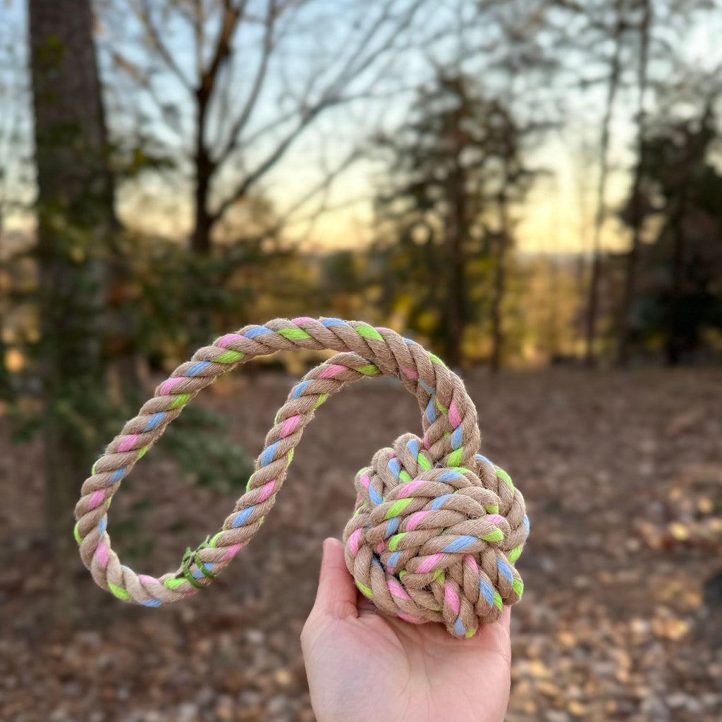 Hand holds a 12.5-inch Rainbow Joy Hemp Rope Tug Toy, natural hemp with blue, pink, and green accents.